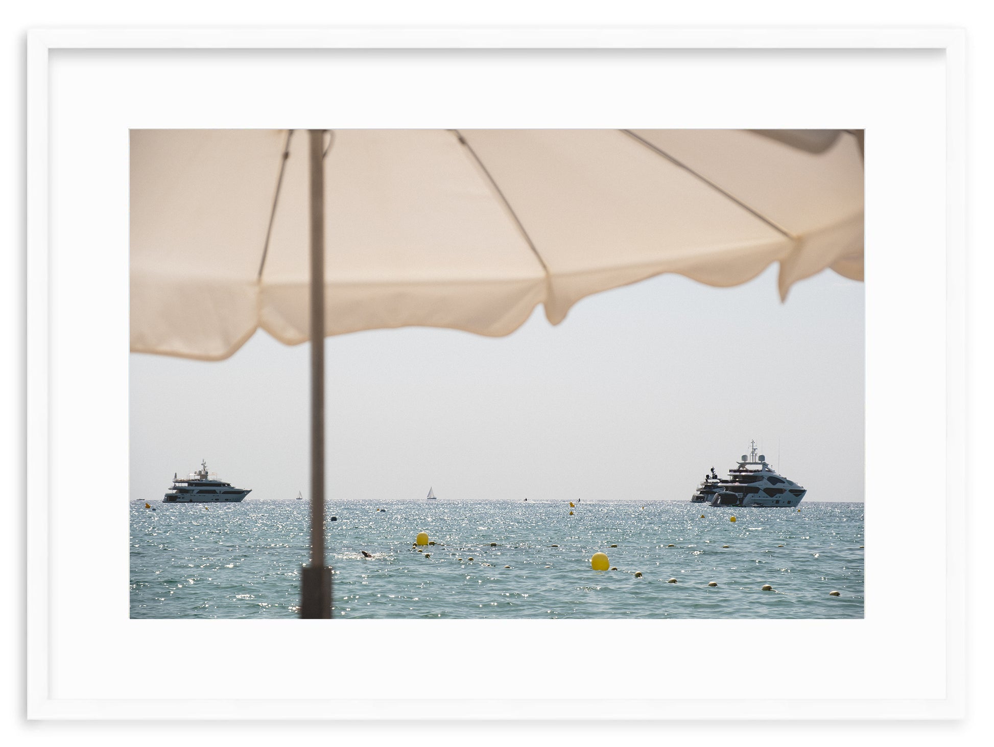 A fine art print of the yachts in front of Club 55 in Ramatuelle, Saint-Tropez, on the French Riviera, taken from the beach under a white umbrella.