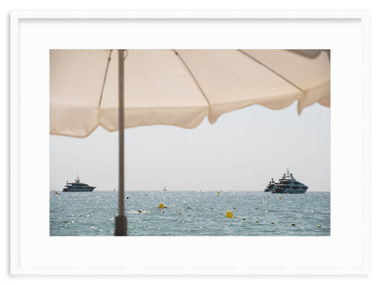 A fine art print of the yachts in front of Club 55 in Ramatuelle, Saint-Tropez, on the French Riviera, taken from the beach under a white umbrella.